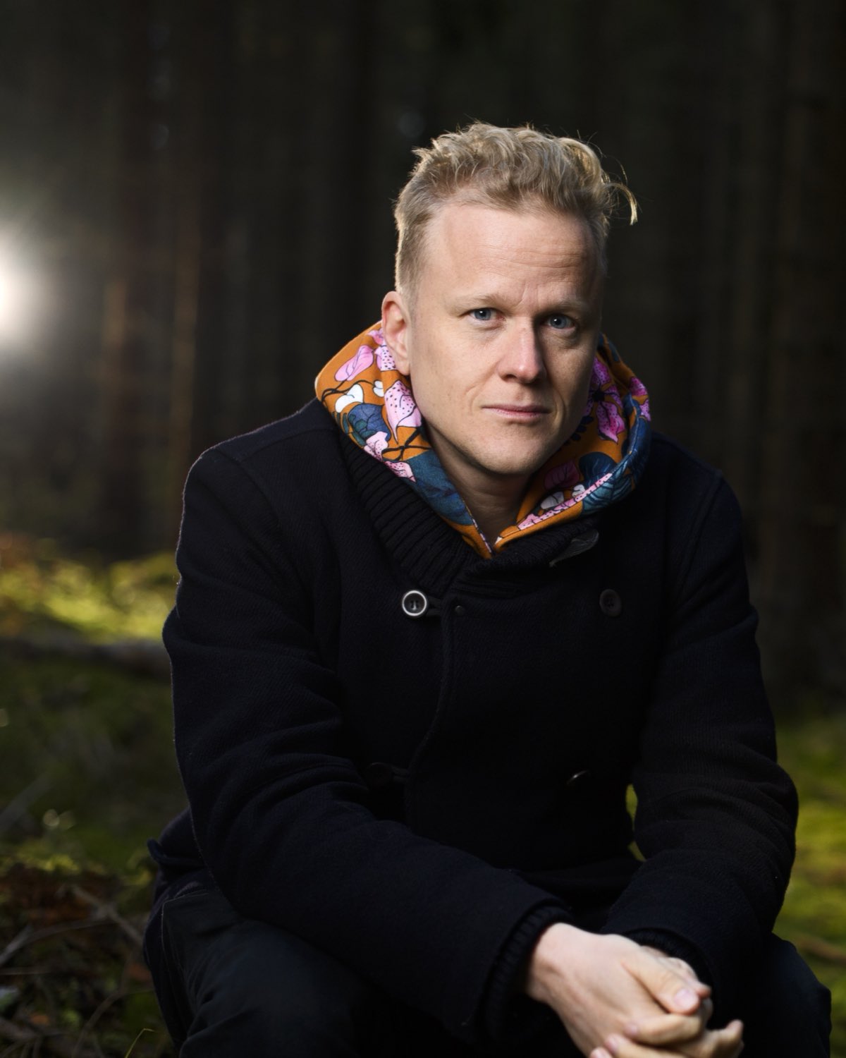 Henrik Ståhl i en mörk skog, med ett ljus mellan träden